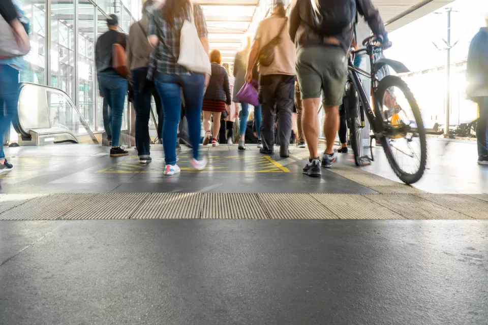 Walkways and escalator at crowded transit station, with one person walking a bike in foreground.